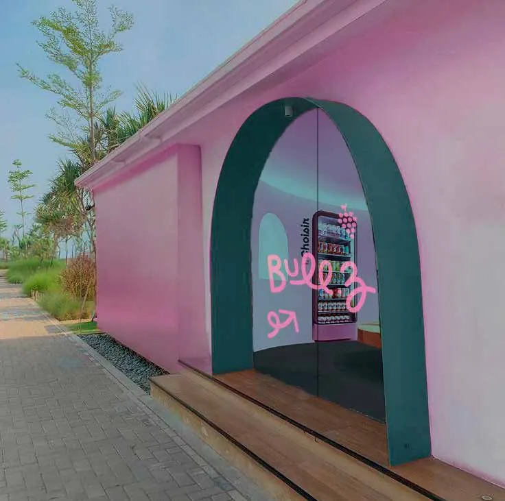 Façade du pop-up store Bull’Z : pavillon rose avec une porte en arche verte, vu de l’extérieur.