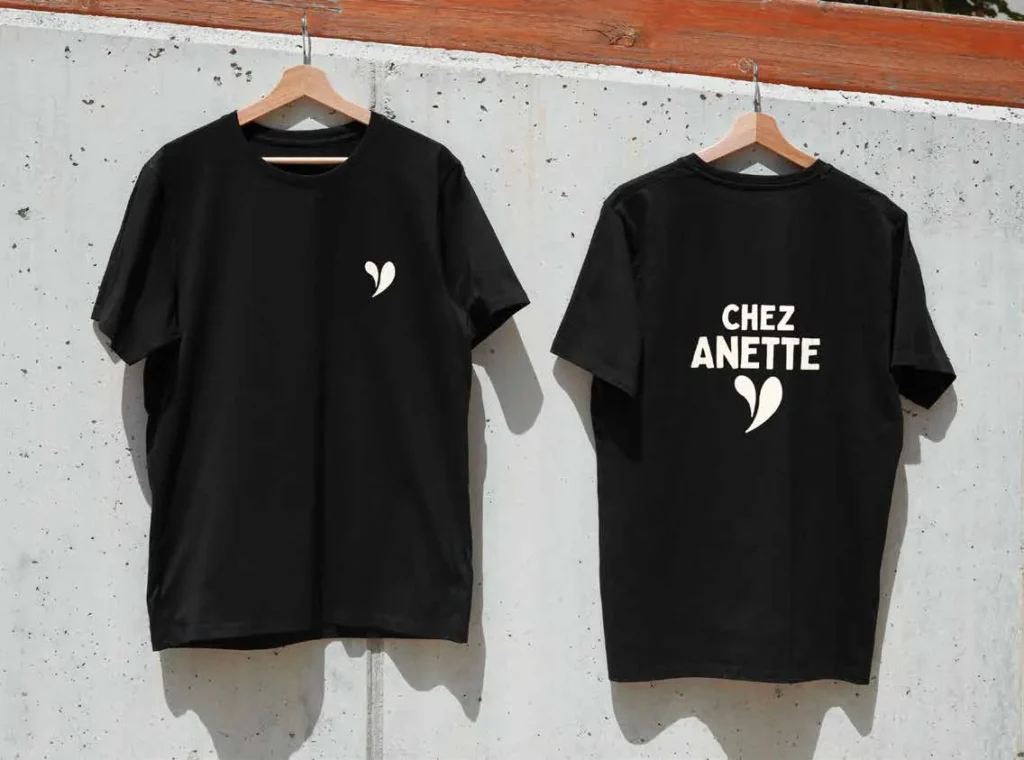 Deux t-shirts noirs suspendus, ornés du logo en forme de cœur stylisé de Chez Anette.